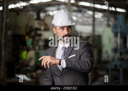 El director de hipster barbudo con sombrero de ingeniero de pie contra el cnc máquina en producción en fábrica Foto de stock