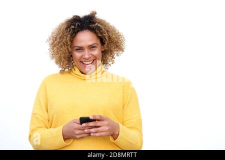 Retrato de una joven afroamericana feliz sonriendo contra aislada fondo blanco con teléfono móvil en la mano Foto de stock