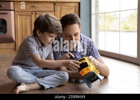 El padre amoroso y el hijo pequeño reparan el coche de juguete juntos