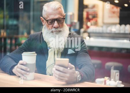 Hombre de negocios senior que usa la aplicación para smartphones mientras bebes café en el bar cafetería - empresario de moda que hace el desayuno - Trabajo, descanso por la mañana y con tecnología