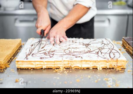 Primer plano de un chef de pastelería cortando un pastel grande en porciones en la pastelería. Metraje 4k de alta calidad.