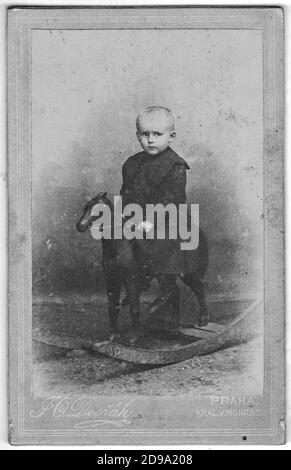 La tarjeta del gabinete Vintage muestra el retrato del niño pequeño. Pequeño niño sentado en un caballo de mecedoras. Moda eduardiana. La foto fue tomada en un estudio de fotos