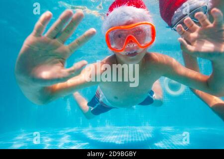 Niño feliz pose bajo el agua con sombrero de Santa Claus en el piscina de buceo y natación
