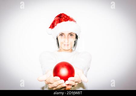 Mujer en traje de Navidad sostiene en dos manos rojo xmas decoración bola brillante regalo. Felicidad y compartir el amor y la esperanza en las celebraciones Foto de stock