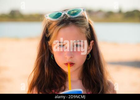 Niña de 10 años en el mar. retrato de un adolescente. chica con gafas de  sol bebe de una pajita una bebida en el mar en la playa.