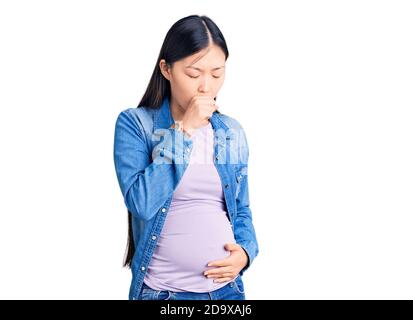 Joven hermosa mujer china embarazada esperando bebé sintiéndose mal y tosiendo como síntoma de resfriado o bronquitis. Concepto de atención médica. Foto de stock