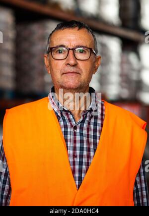 Trabajador adulto hombre naranja de alta visibilidad de cerca de estanterías de almacén y mirando la cámara Fotografía de stock - Alamy