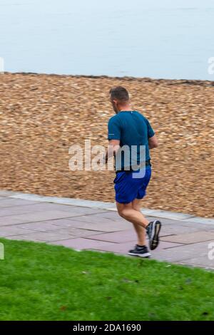 hombre de mediana edad corriendo a lo largo de un camino en la playa o. junto al mar para mantenerse en forma y saludable Foto de stock