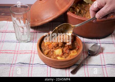 Sirve en un cuenco de cerámica un delicioso estofado casero de lentejas, tomate, chorizo español, carne y patatas. Foto de stock