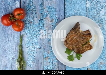 un trozo de carne de cerdo deliciosa. filete frito en un plato sobre un fondo de madera. un trozo de carne frita con tomates y un ramito de romero. Foto de stock