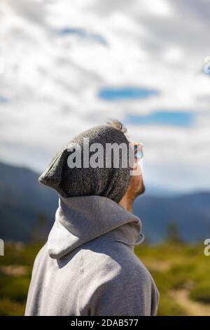 Joven hombre blanco de detrás con gafas de sol en hermoso natural entorno rodeado de montañas con vistas al cielo nublado