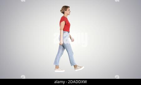 Mujer en camiseta roja, vaqueros y zapatillas de deporte caminando en gradiente bac