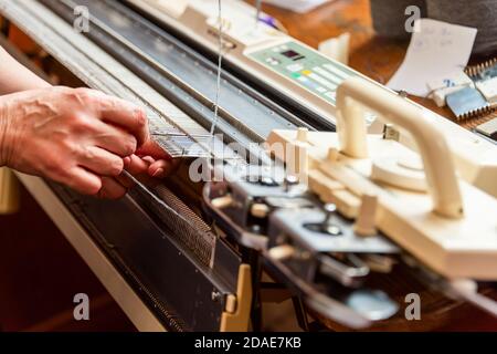 Mujer trabajando con las manos en la máquina de tejer en casa. Pequeña empresa Foto de stock