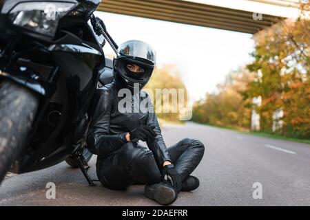 Biker chica en traje negro se sienta apoyado en una motocicleta