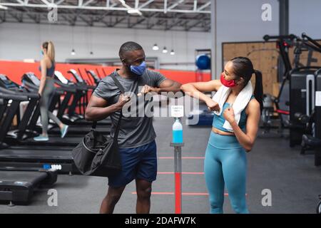 Encaje hombre afroamericano y encaje mujer caucásica saludando a cada uno otros tocando los codos en el gimnasio