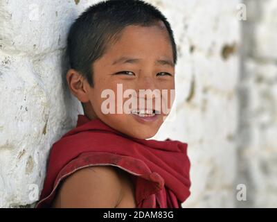 Lindo pequeño monje budista tibetano en bata de granate sonríe para la cámara dentro del monasterio de Tawang. Foto de stock