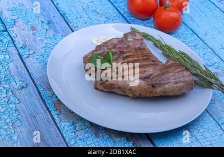 un trozo de carne de cerdo deliciosa. filete frito en un plato sobre un fondo de madera. un trozo de carne frita con tomates y un ramito de romero. Foto de stock
