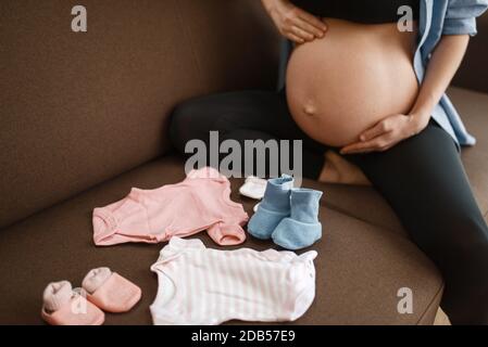 La mujer embarazada con vientre prepara ropa para recién nacidos casa. Embarazo, calma en el período prenatal. Mamá expectante descansando en dormitorio, más sana Fotografía de stock - Alamy