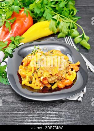 Pollo guisado con tomates, pimientos rojos y amarillos y queso en un plato sobre servilleta, tomillo, perejil y ajo sobre fondo de madera
