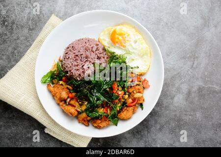 Pollo cocinado con el verde de la albahaca, servido con arroz cocido y huevo frito, caliente y picante del plato con hojas de albahaca. Foto de stock