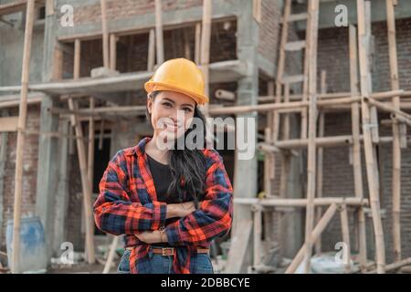 hermosas contratistas asiáticas con cascos de seguridad con manos cruzadas en el fondo de la construcción del edificio