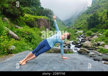 Yoga al aire libre - hermosa mujer deportiva en forma haciendo yoga asana Vasisthasana - posición de tabla lateral en la cascada tropical Foto de stock