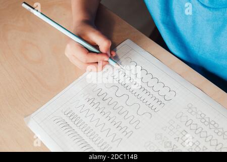 Primer plano de niño lindo haciendo ejercicios de escritura. Niño Use lápiz para dibujar líneas. Concepto de educación infantil Foto de stock