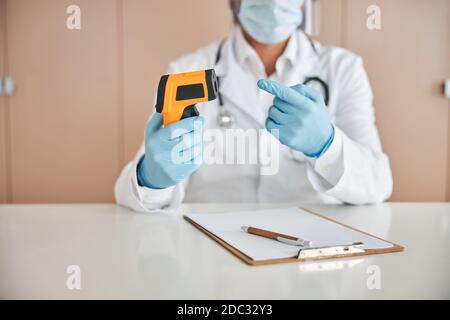 Médico masculino demonizar un termómetro moderno sin contacto Foto de stock