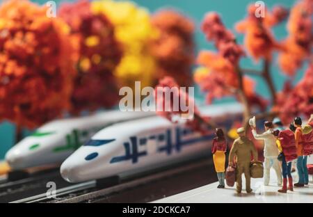 Figurillas de juguete en miniatura de mujer sola esperando en una plataforma de tren de alta velocidad en otoño o otoño concepto de temporada - filtro de tono cálido aplicado. Foto de stock