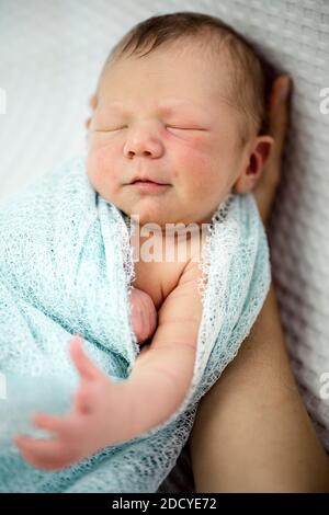 Lindo bebé recién nacido dormido envuelto en azul tumbado la mano de la madre Foto de stock
