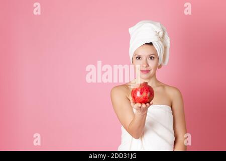 se mofa, retrato de una hermosa joven con una toalla en su cabeza y en su cuerpo sosteniendo una granada a nosotros, aislada sobre un fondo rosa Foto de stock