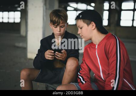 Grupo de adolescentes niños en el interior de un edificio abandonado, utilizando un smartphone. Foto de stock