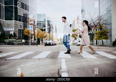 Hombre agarrando las manos con la mujer mientras cruzaba el camino en la ciudad