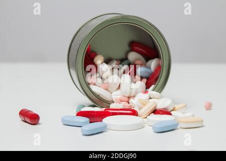 Una lata volcada sobre una mesa blanca y muchas pastillas y cápsulas. Exceso de drogas y productos químicos. Foto de stock