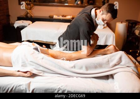 Terapeuta profesional haciendo un masaje profundo a un cliente masculino en el salón de Spa. Trabajando en la parte inferior del cuerpo Foto de stock