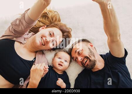 Madre y padre y su pequeño y lindo hijo acostado la alfombra