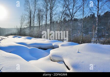 Curvas suaves y extrañas de superficie de nieve cerca del bosque de invierno. Relieve retorcido de la superficie nevada, hermosa y sinuosa nevadas.Belleza de las líneas nevadas, Foto de stock