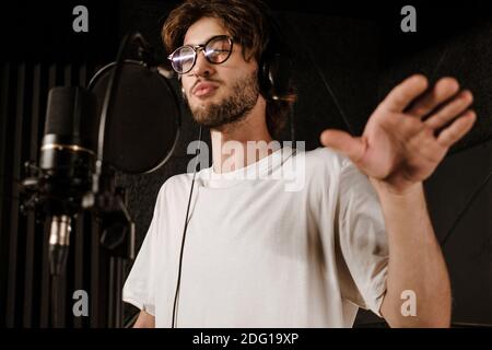 Retrato de un joven cantante en auriculares cantando durante el disco nuevo canción en el estudio