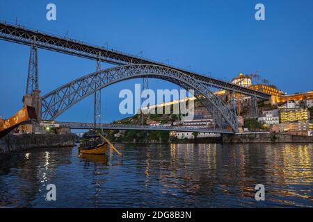 Clip angular bajo del Puente Luis I durante el crepúsculo de la noche en Oporto, Portugal. Barco rabelo de madera en primer plano Foto de stock