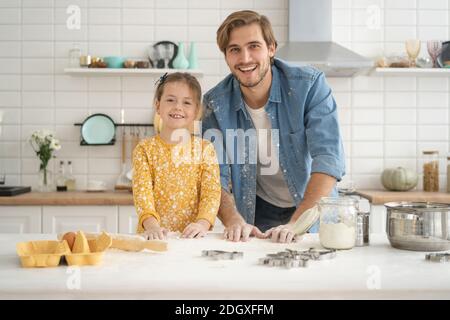 Padre alegre y la hija divertirse amasando la masa en la mesa de la cocina, hornear juntos Foto de stock
