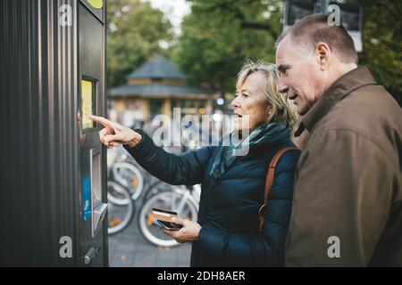 Hombre mayor con mujer haciendo el pago a través de la tarjeta de crédito en estación de alquiler de bicicletas Foto de stock