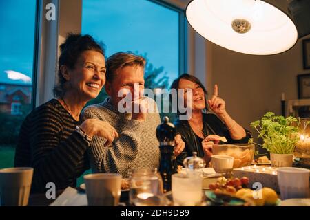 Feliz mujer mayor y hombre sentado en una mesa de comedor iluminada mientras disfruta de la cena