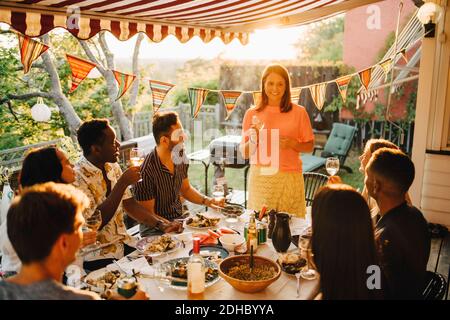 Mujer levantando pan tostado mientras disfruta de la comida con amigos en la cena fiesta Foto de stock