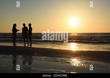 Silueta de tres personas de pie en la playa Clearwater hablando al atardecer. Foto de stock