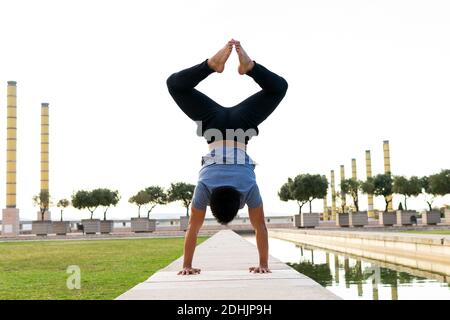 Vista al revés de un equilibrio masculino irreconocible en las manos Adho Mukha Vrksasana mientras hace yoga en la alfombra en el parque Foto de stock