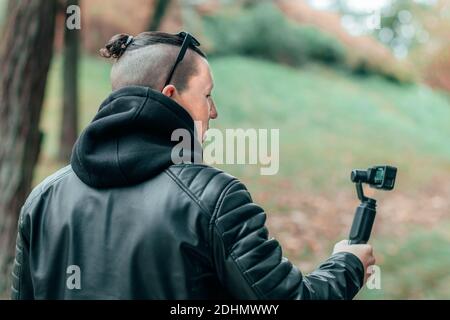 Blogger en ropa negra y gafas de sol haciendo video usando la acción Cámara  con Estabilizador Gimbal en Autumn Park Fotografía de stock - Alamy