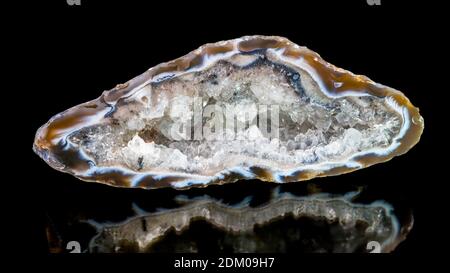 Quartz crystal inside large geode. Agate gem cross-section with reflection on black background. Clear crystalline mineral in hollow cut precious stone.