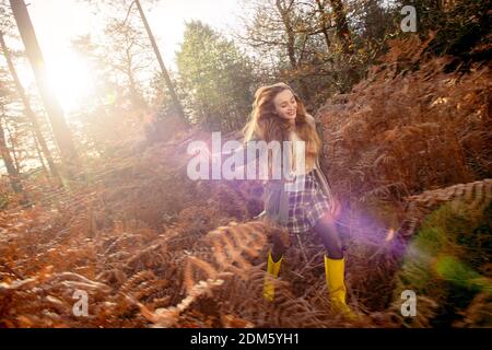Una mujer joven y natural (20 años) corre por los helechos otoñales y se divierte en un entorno de bosque con una sensación de movimiento en un día soleado.