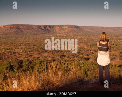 Mujer turística de vuelta a cámara en un mirador en la carretera del río Gibb con vistas a la cordillera Wunaamin Miliwundi, Kimberley, Australia Occidental.