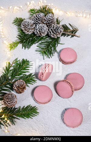Macarones de higo bellamente dispuestos en una mesa blanca, winterly decorado con ramas de abeto y conos de pino, una cadena Lichter brilla en el fondo Foto de stock